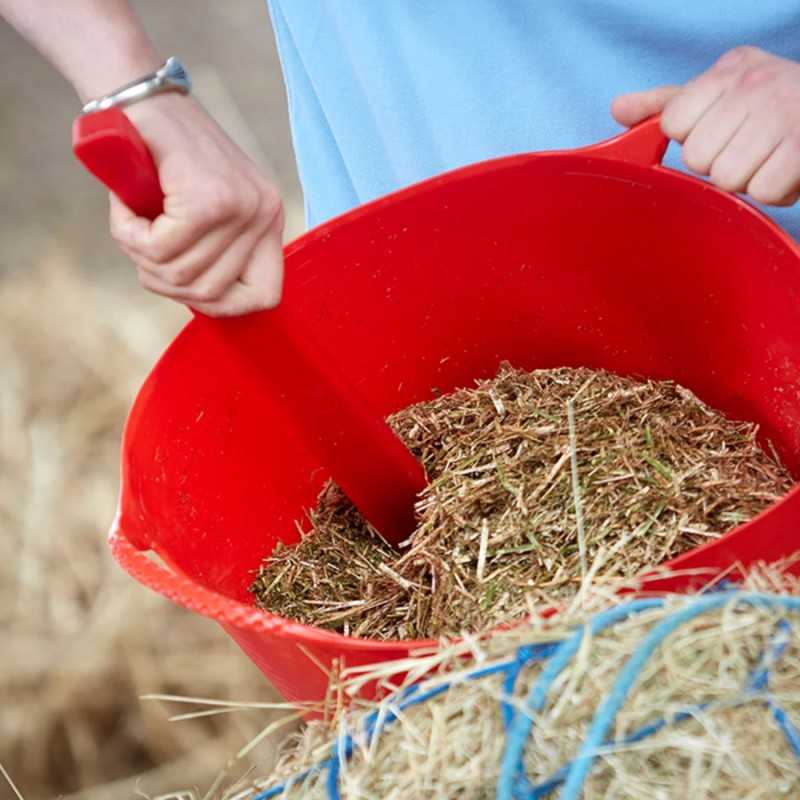 Balde vermelho de plástico com ração à base de palha e pá vermelha em ambiente agrícola