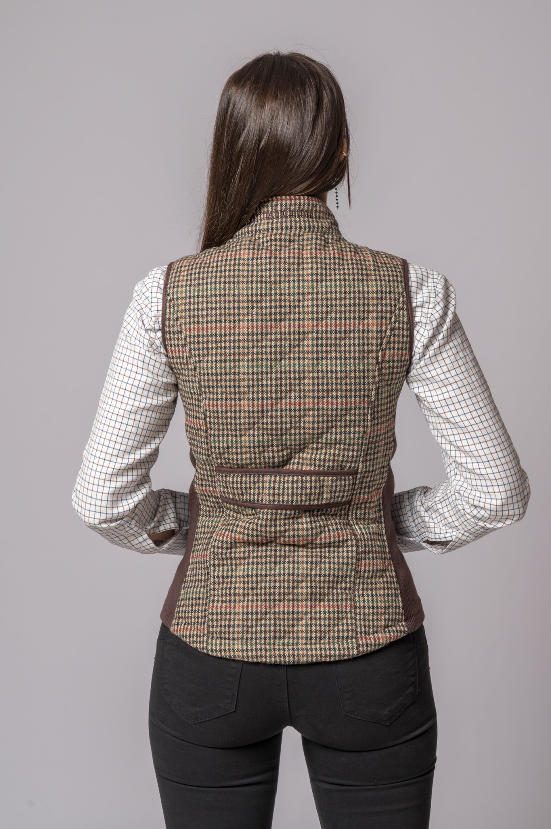 Modelo usando colete xadrez bege com camisa branca quadriculada e calças pretas visto de costas