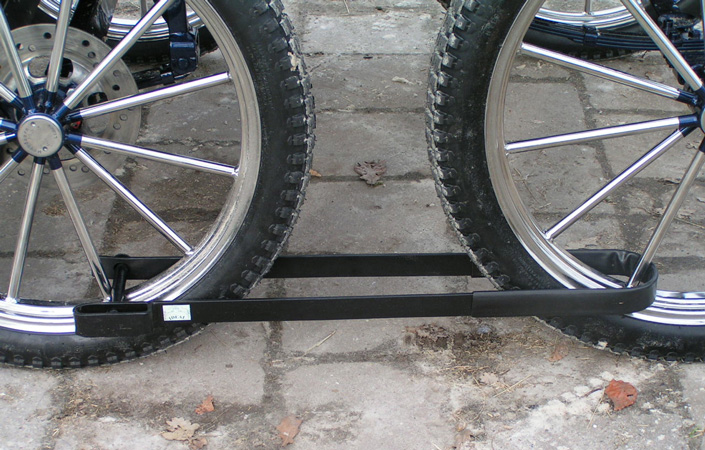 Duas rodas de bicicleta ligadas por barra preta sobre piso de cimento