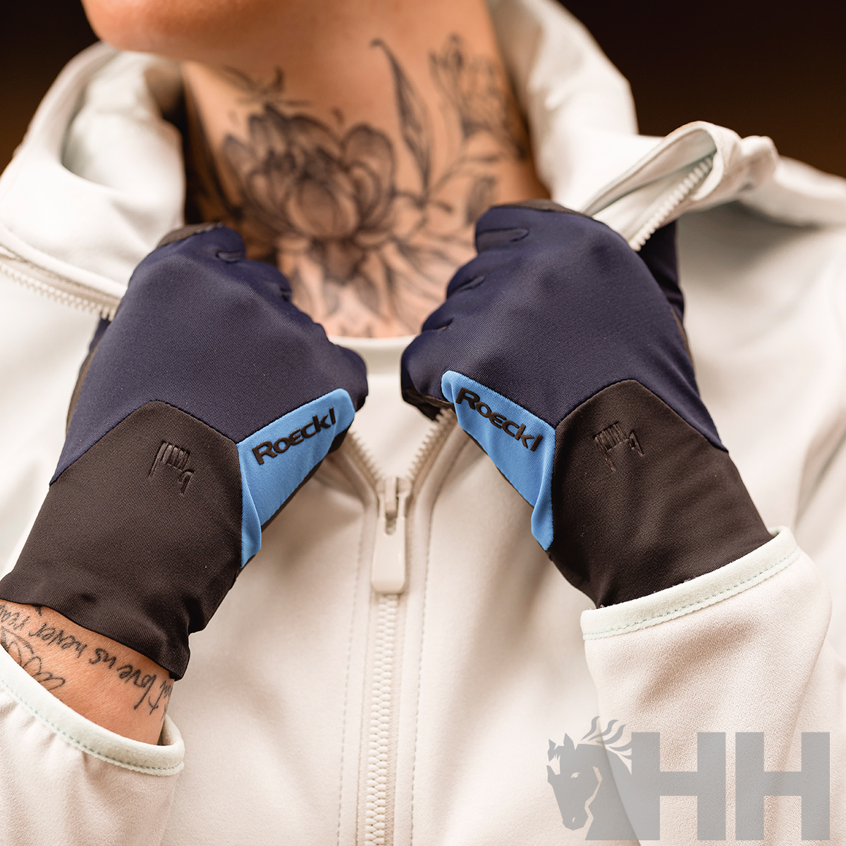 Luvas desportivas Roeckl azul e preto com casaco branco e tatuagens visíveis