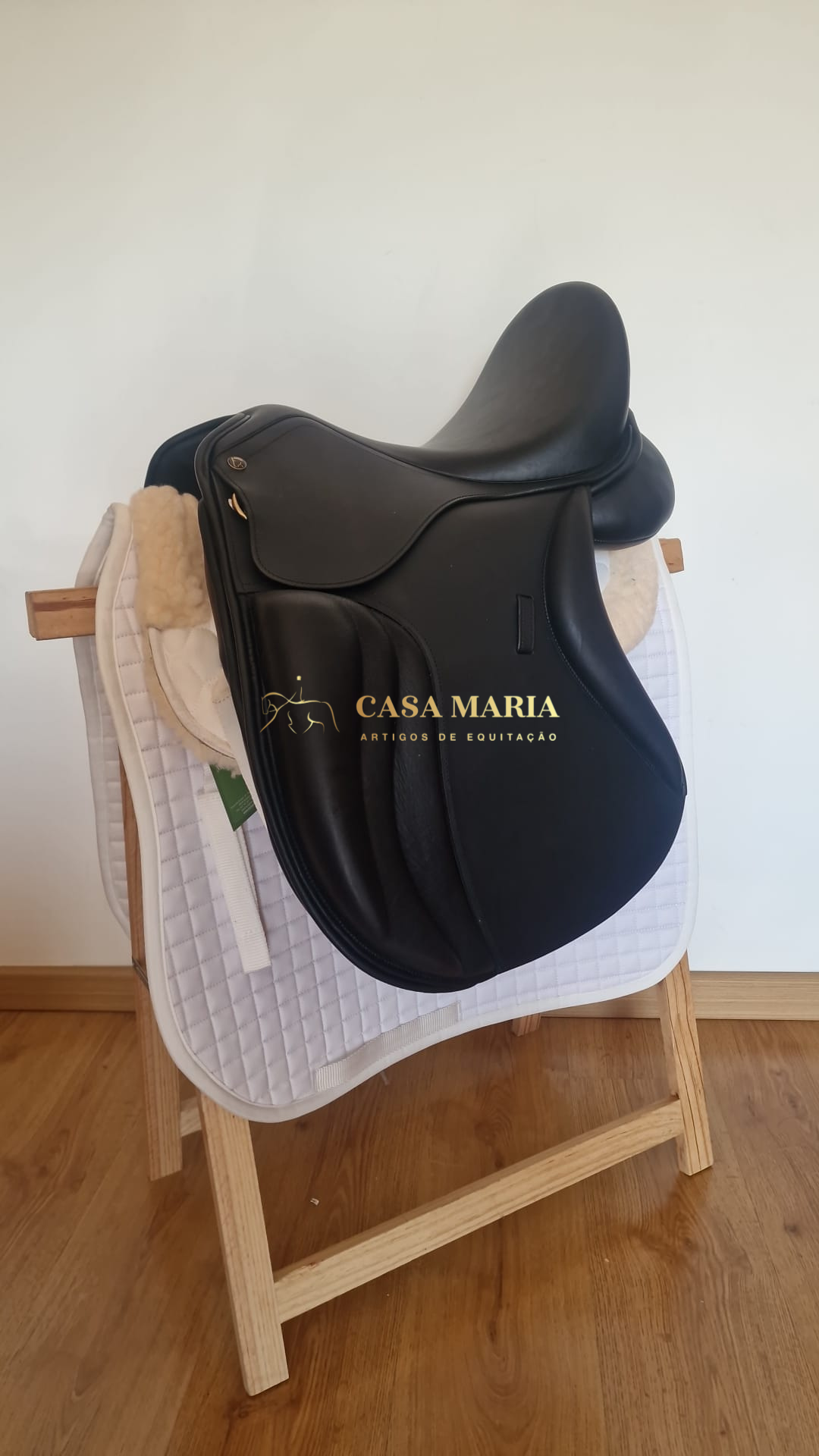 Sela de equitação preta em couro sobre manta branca acolchoada num suporte de madeira