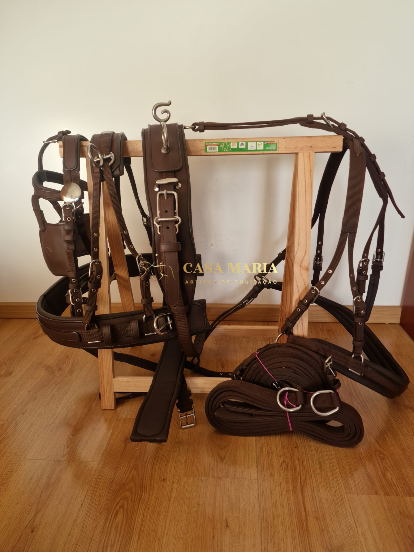 Arnês de sela castanho em couro com fivelas metálicas sobre suporte de madeira