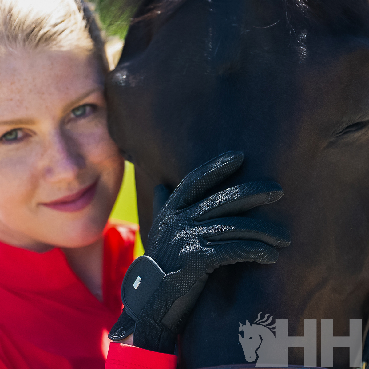 Mulher com luvas pretas e casaco vermelho tocando cavalo preto