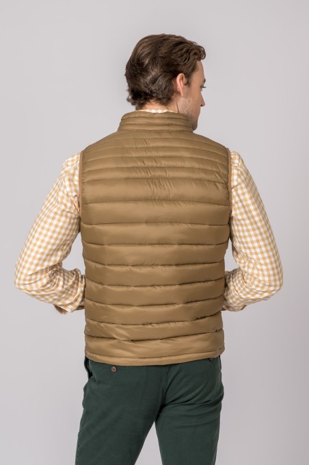 Homem de costas usando colete acolchoado castanho claro, camisa xadrez bege e branco e calças verdes escuras