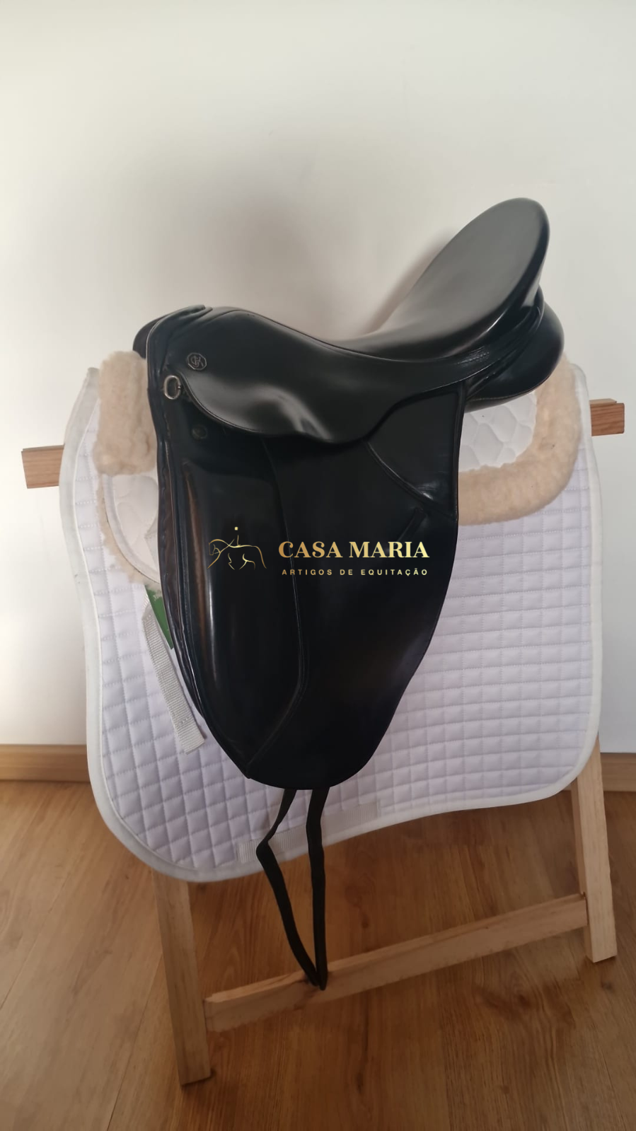 Sela de equitação preta em couro sobre alforge branco acolchoado, montada em suporte de madeira