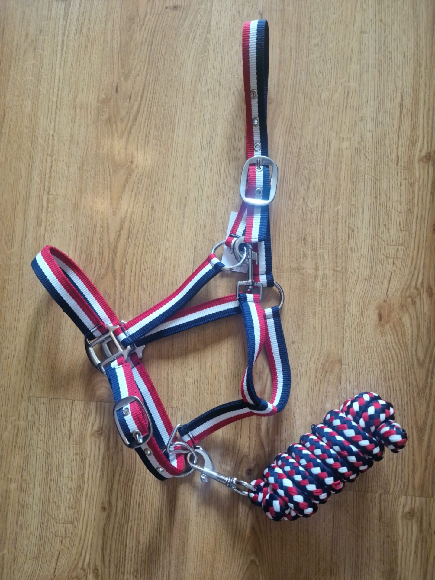 Cabresto e guia para cavalo em tecido com cores vermelho, branco e azul sobre chão de madeira