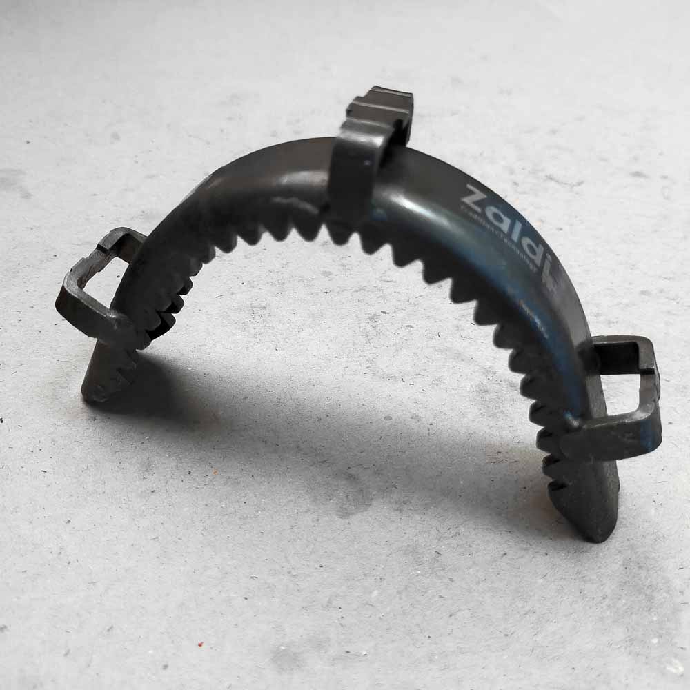 Pomo metálico preto com dentes em meia-lua e três encaixes sobre superfície cinza