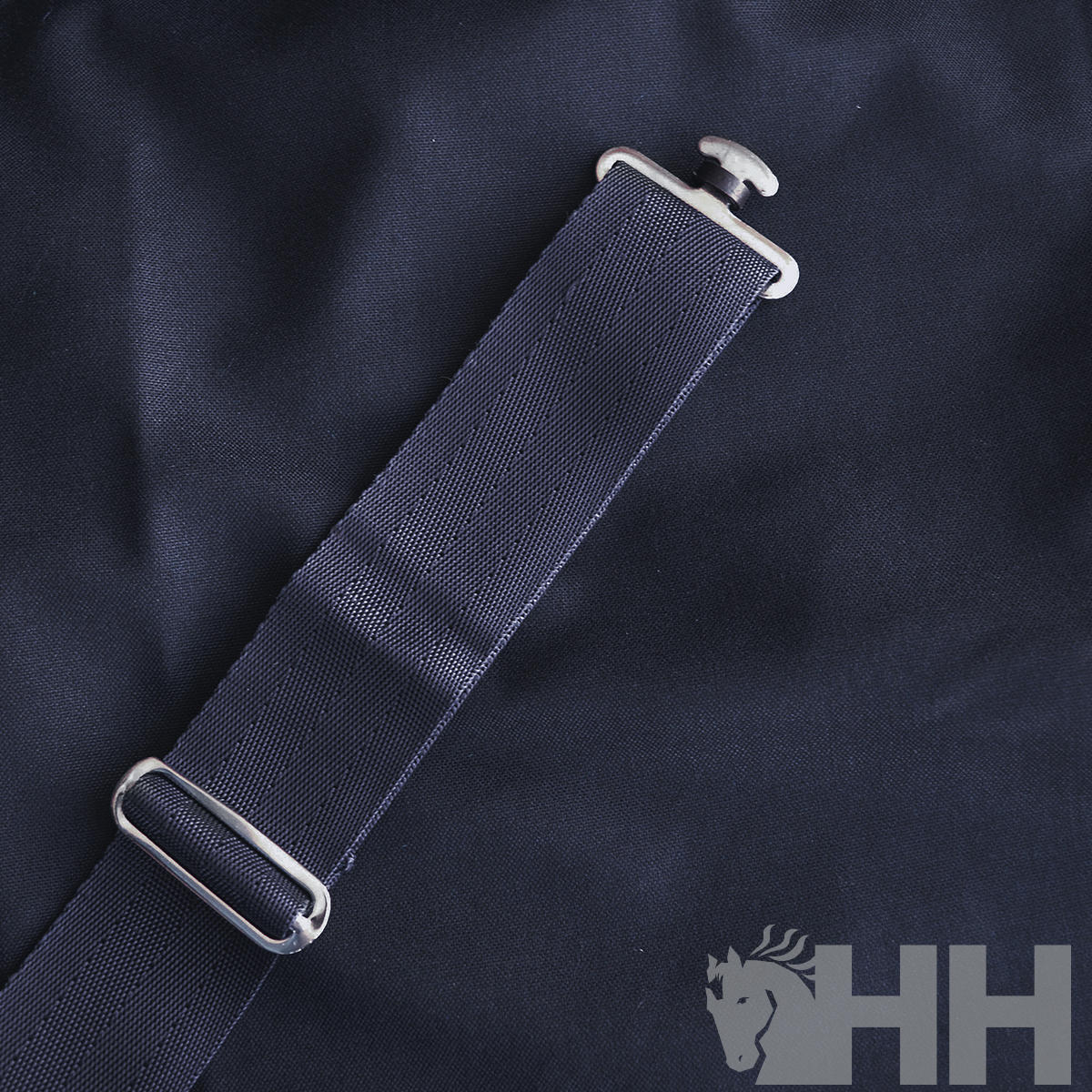 Cinta azul escura com fivela metálica sobre tecido azul com logotipo 'HH' e cavalo branco.