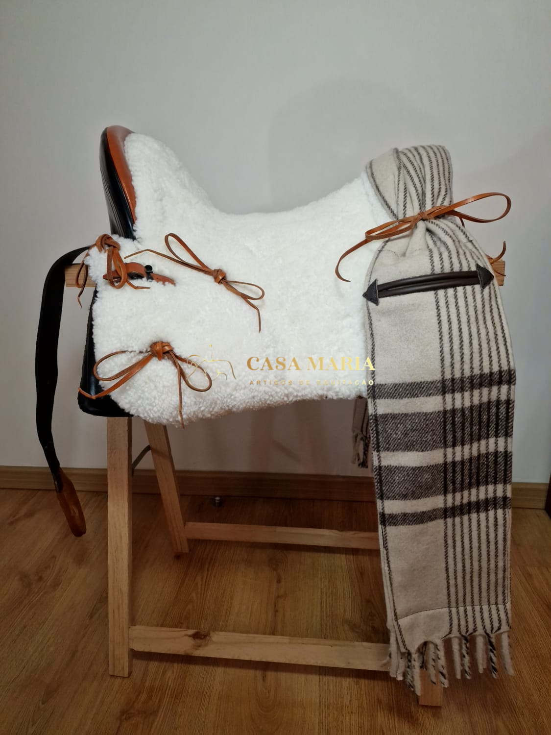 Sela branca peluda com couro e fitas, manta xadrez pendurada em estrutura de madeira