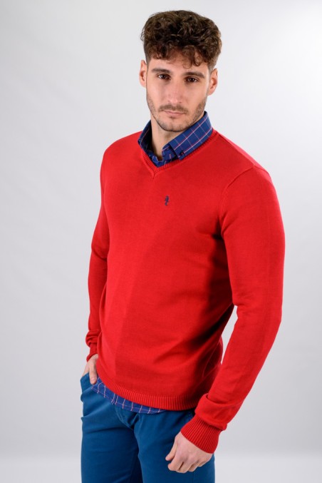 Homem com camisola vermelha e camisa azul xadrez, calças azuis, fundo cinzento