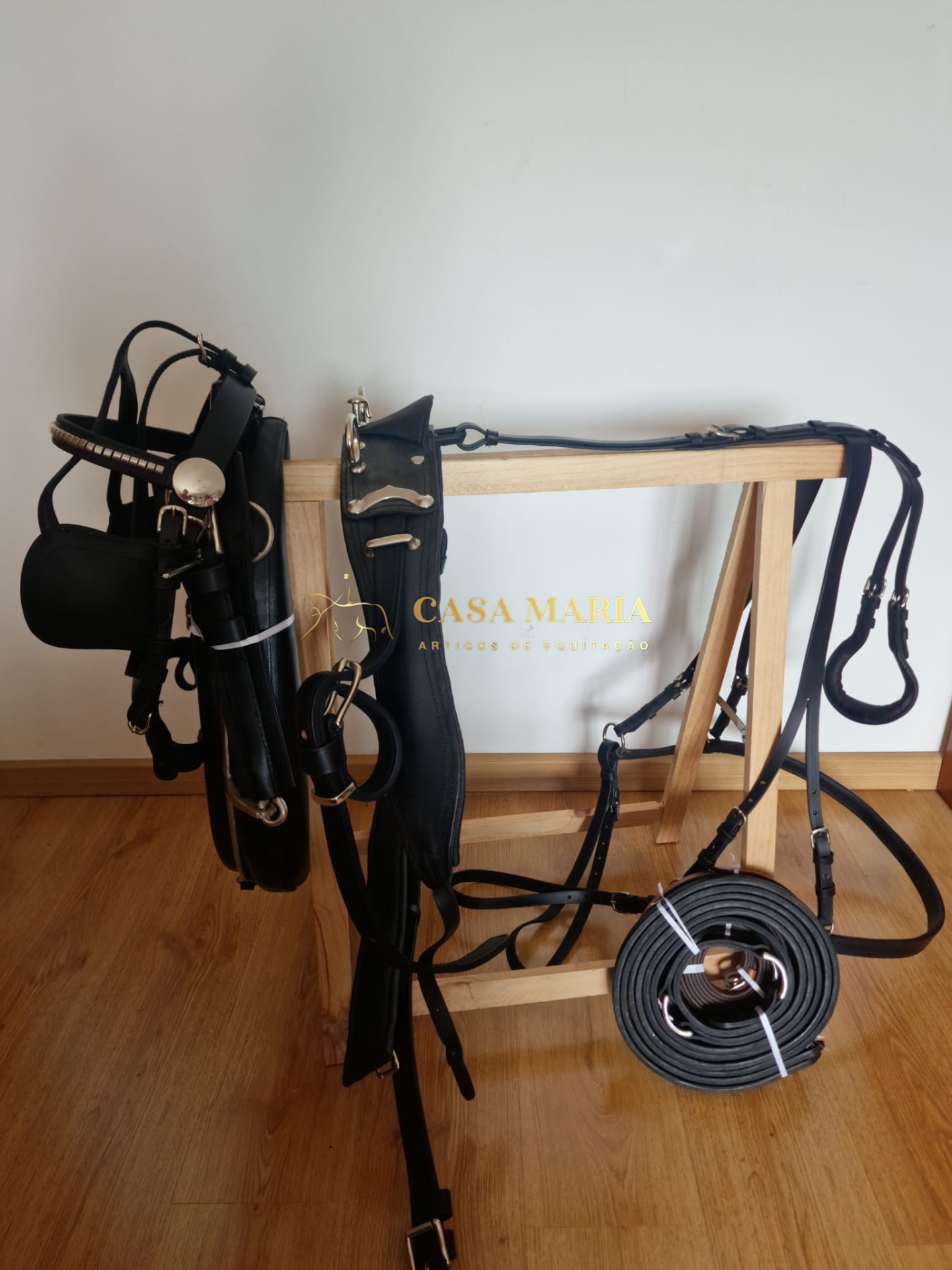 Acessórios de equitação em couro preto pendurados num suporte de madeira.