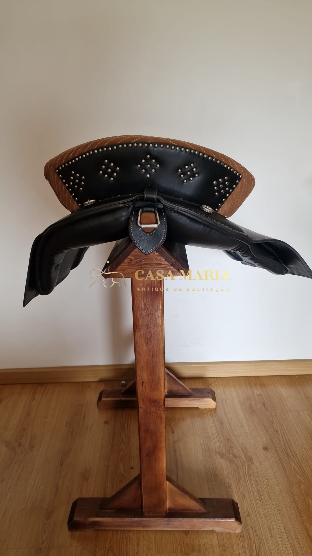 Sela de equitação preta com rebites num suporte de madeira