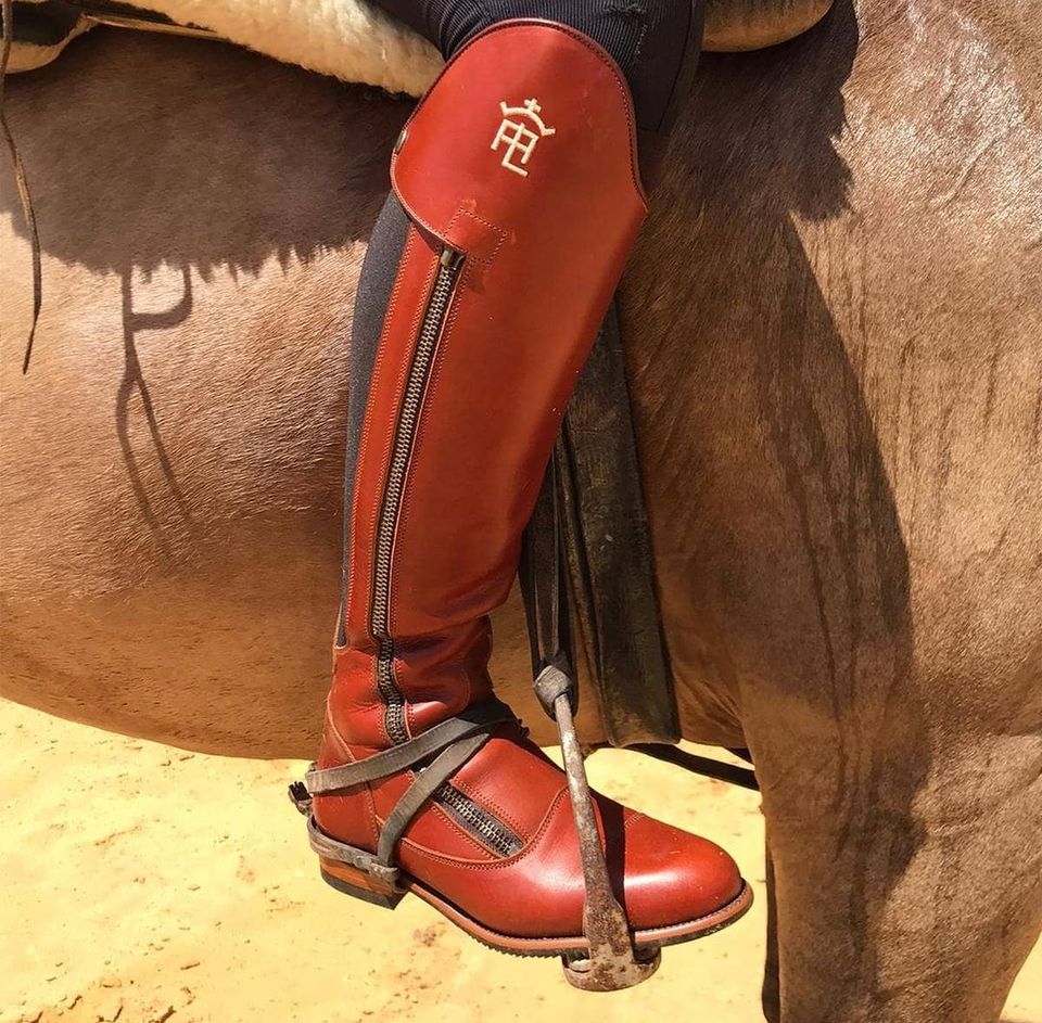 Bota de equitação vermelha com fecho ao lado usada por cavaleiro no cavalo castanho