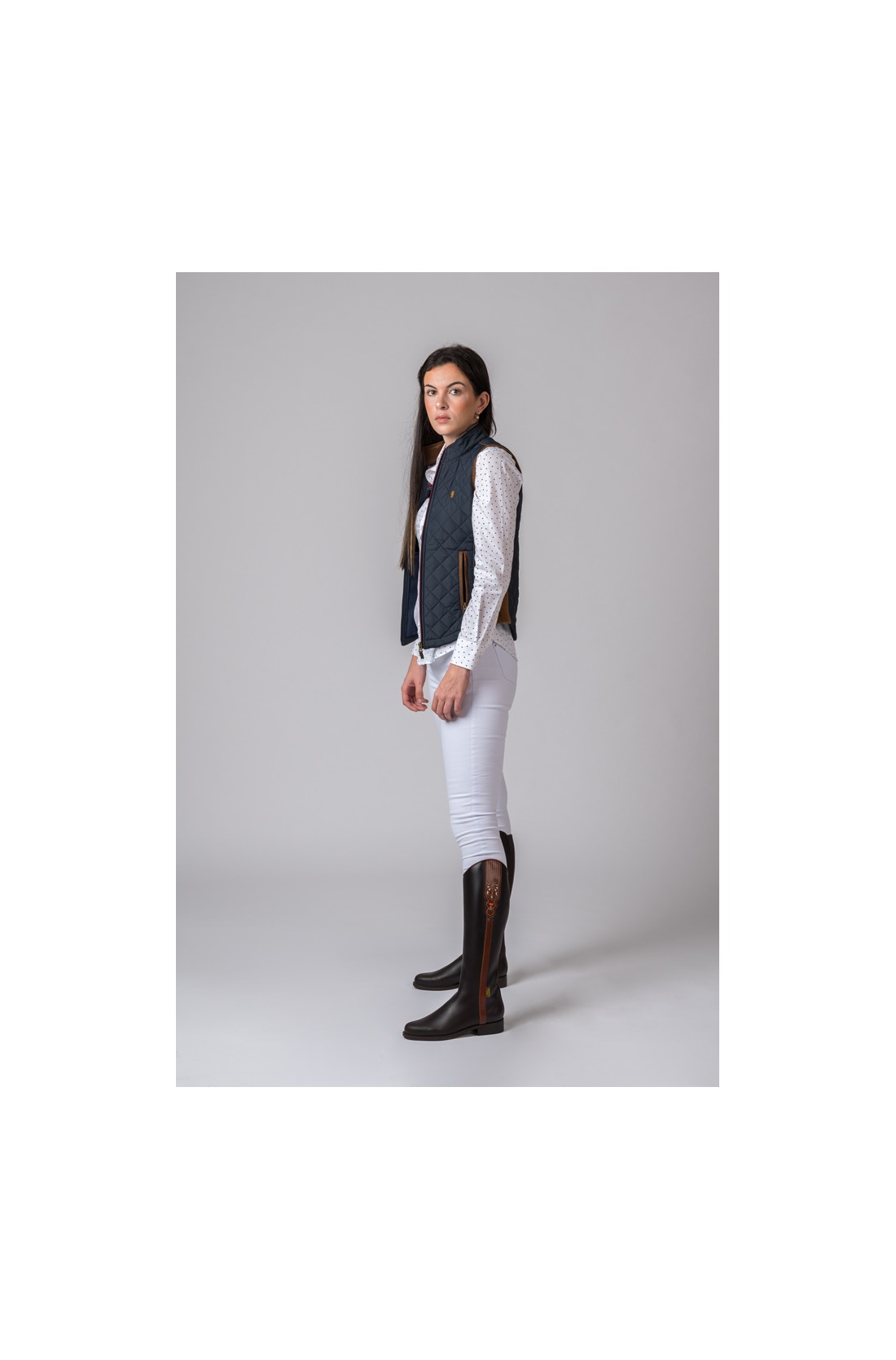 Mulher com colete azul, camisa branca, calças brancas e botas pretas