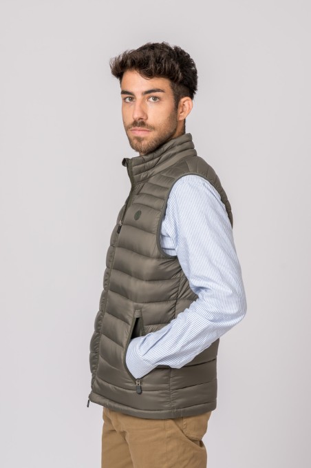 Homem com colete acolchoado verde-acinzentado, camisa azul clara às riscas e calças castanhas