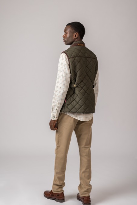 Homem de costas com colete verde escuro, camisa branca às riscas, calças bege e sapatos castanhos