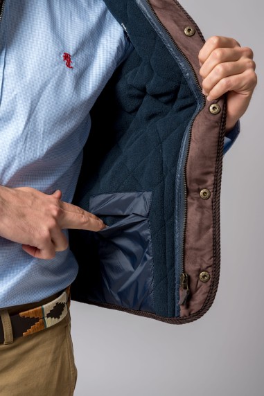 Casaco castanho aberto mostrando interior acolchoado azul com bolso interno e pessoa vestindo camisa azul clara.