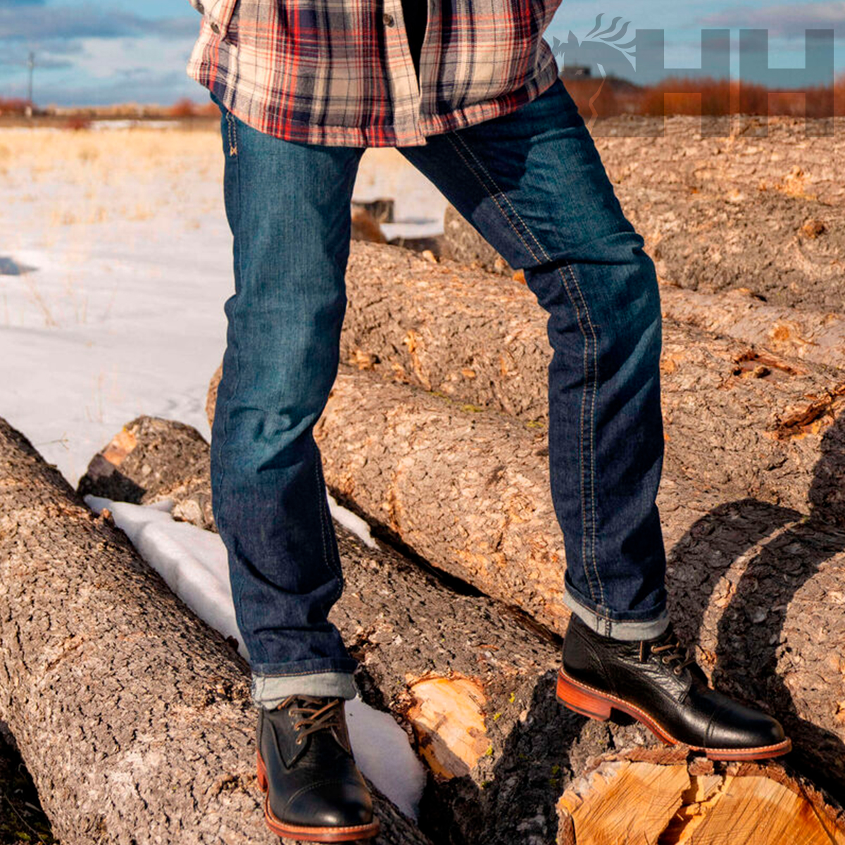 Calças de ganga azuis com sapatos pretos sobre troncos de árvore cortados.