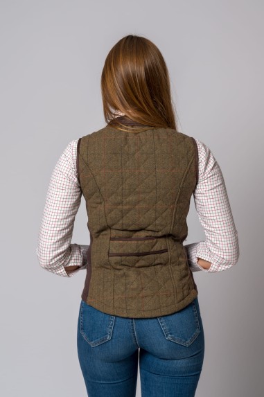 Mulher vista de costas com colete acolchoado xadrez castanho e camisa xadrez branca com calças jeans azuis.