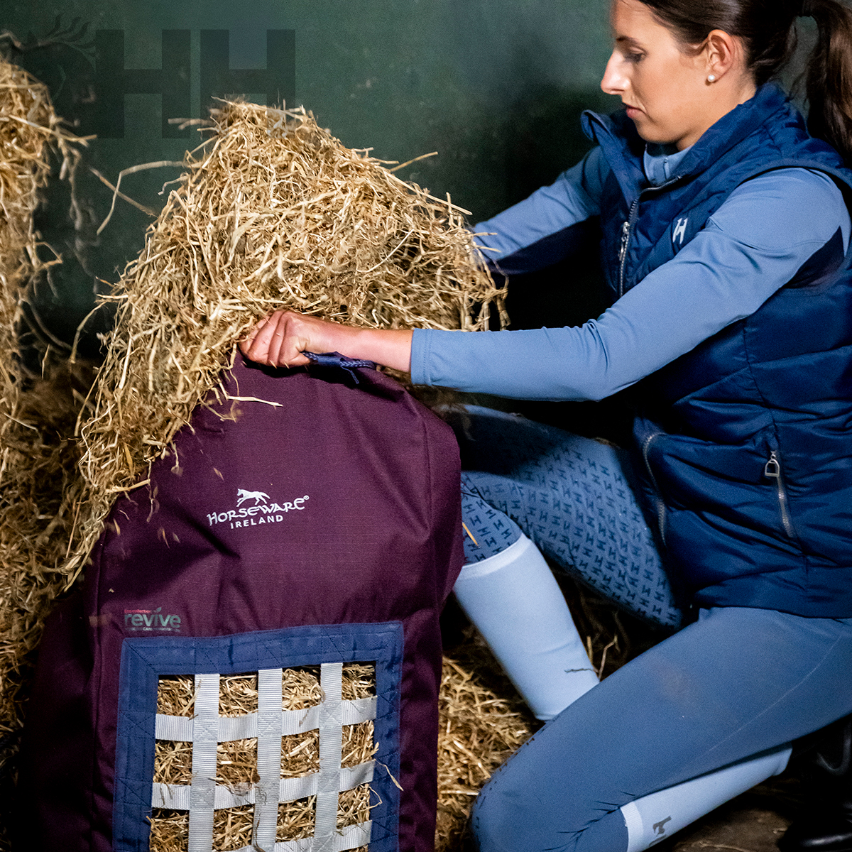 Mulher a colocar feno em saco Horseware Ireland bordeaux com rede branca no estábulo