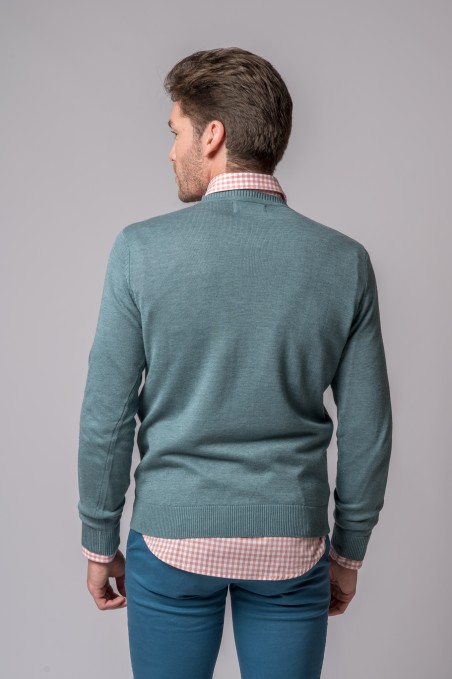 Homem de costas a usar casaco de malha azul-petróleo com camisa xadrez rosa e branco e calças azul-turquesa