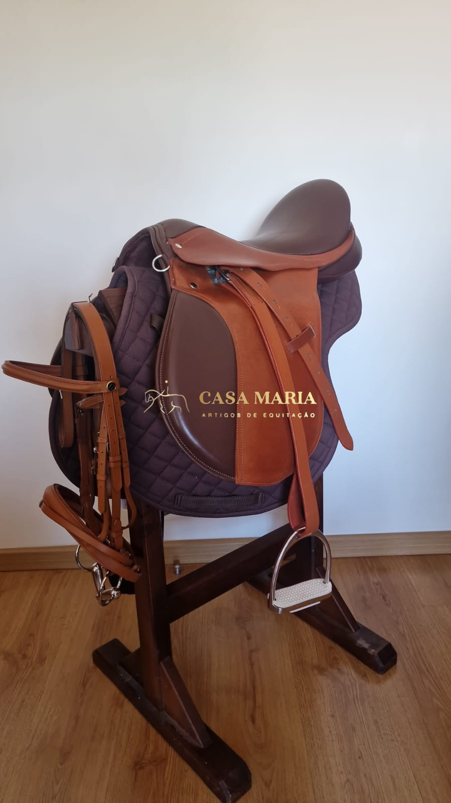 Sela de equitação castanha em couro sobre almofada acolchoada roxa com suporte de madeira