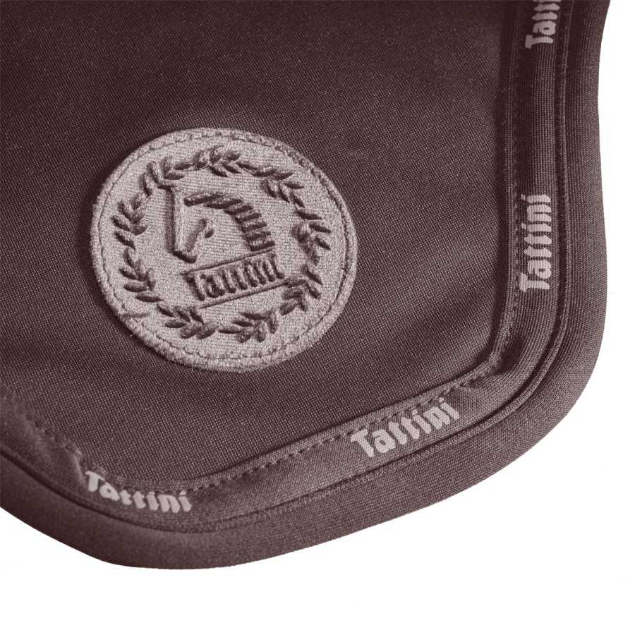Detalhe de tecido castanho com patch bordado de cavalo e borda com palavra Tattini