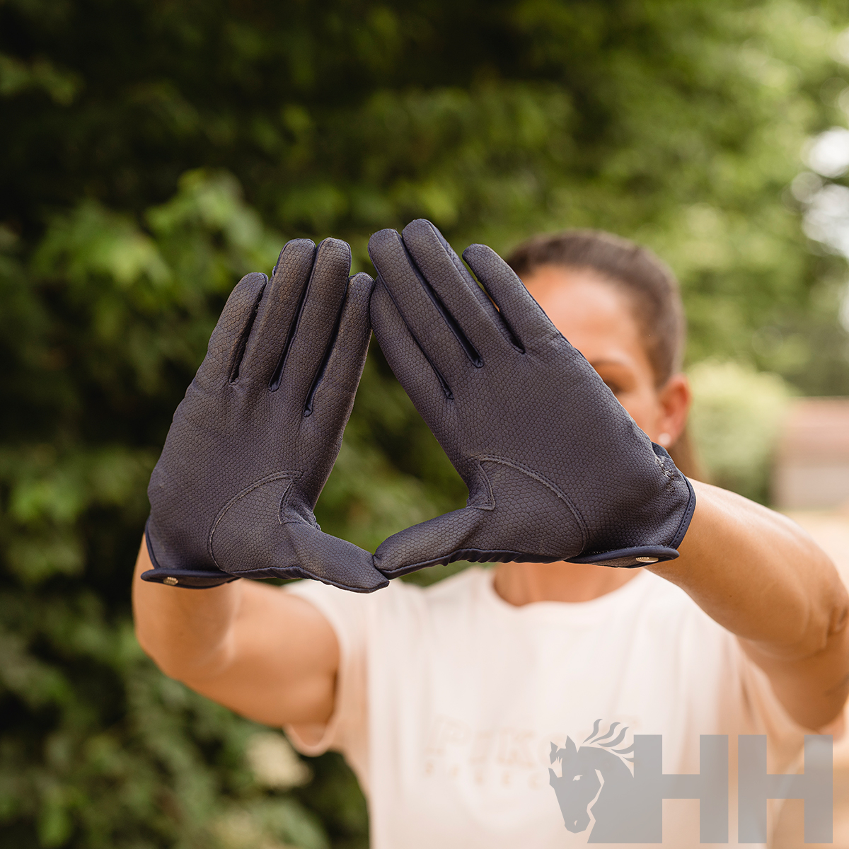 Luvas pretas texturizadas com botão metálico ao punho em fundo natural.