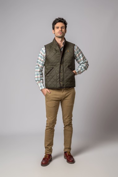 Homem com colete acolchoado verde, camisa riscada, calças castanhas e sapatos castanhos