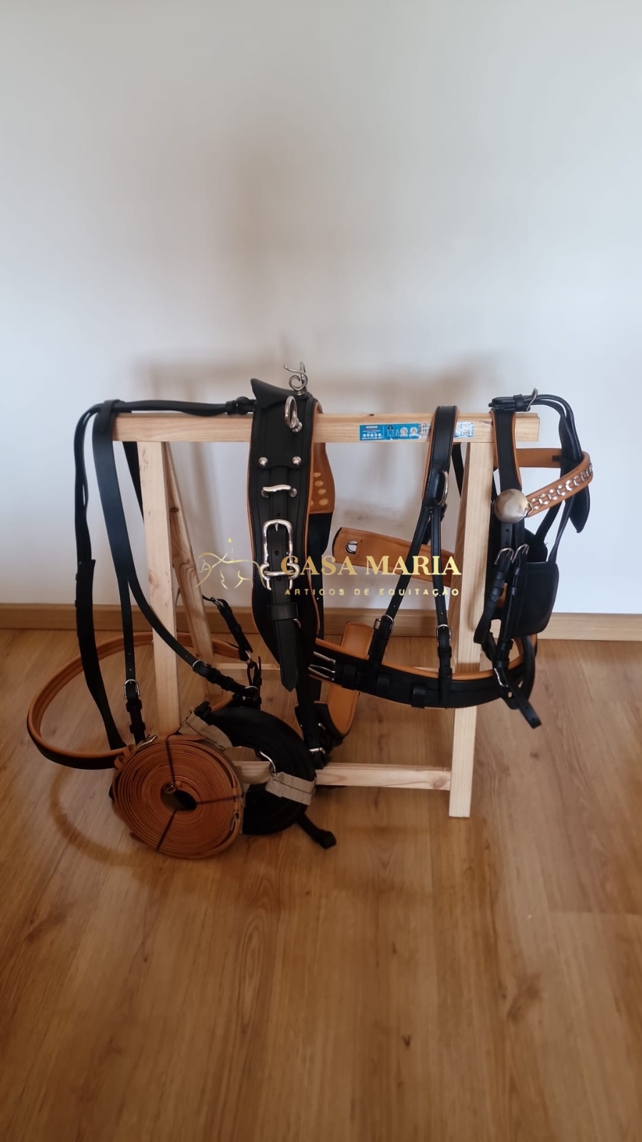 Conjunto de arreios de couro preto e castanho pendurado em estrutura de madeira