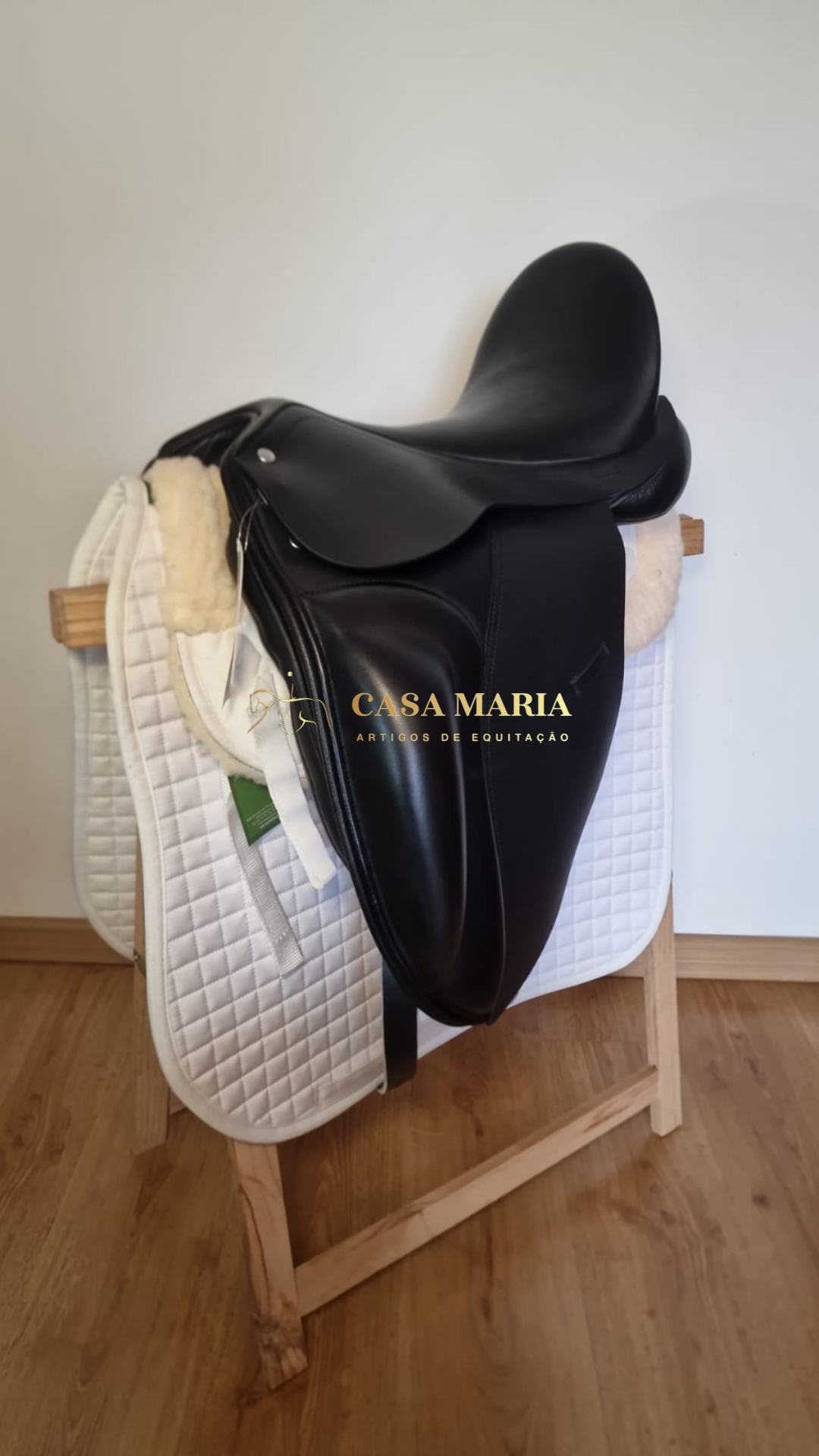 Sela de equitação preta em couro sobre manta branca e suporte de madeira