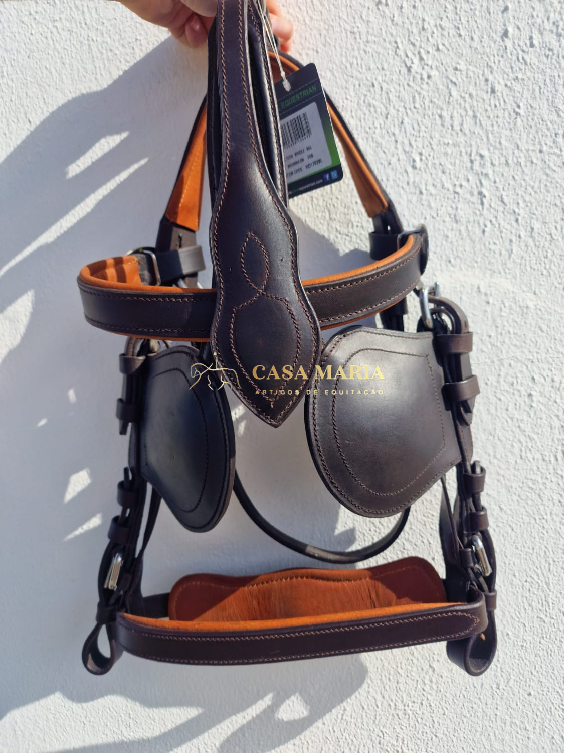 Cabeçada de equitação em couro castanho escuro pendurada numa parede