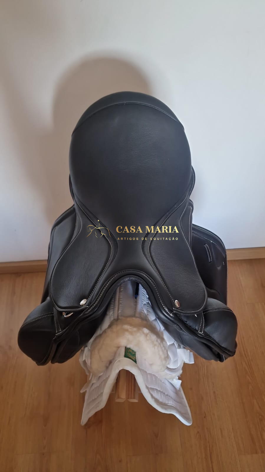 Sela de equitação preta em couro com manta branca sobre suporte de madeira