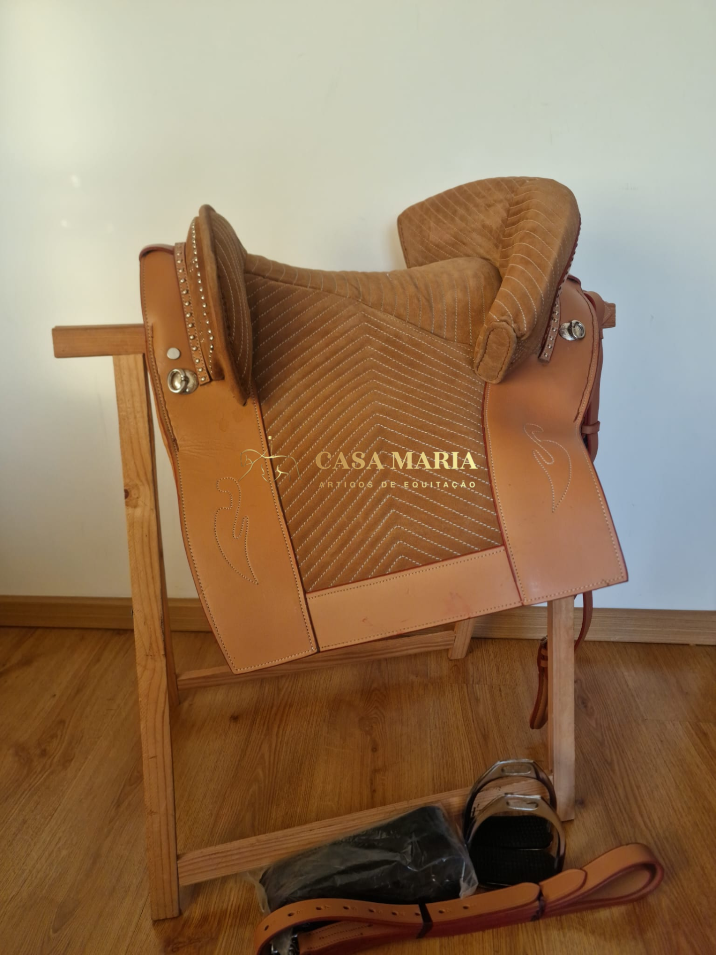 Sela de equitação castanha com acessórios num suporte de madeira