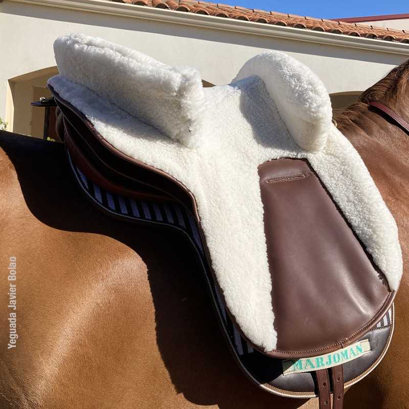 Sela de equitação em couro castanho com almofadado branco felpudo montada num cavalo castanho