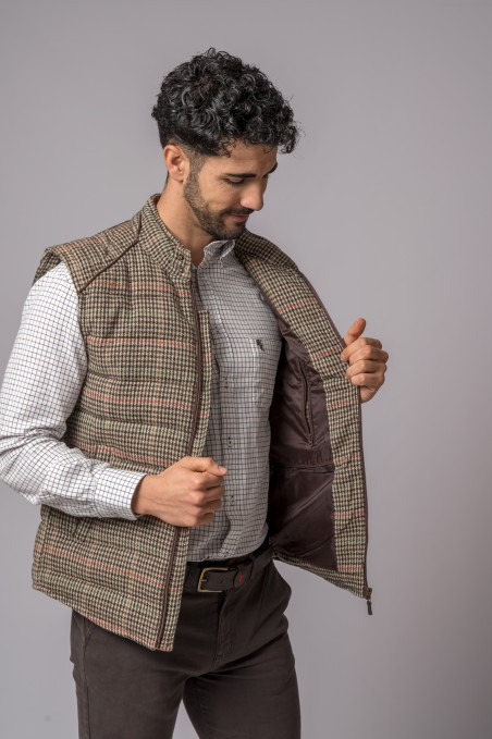 Colete masculino xadrez castanho e bege com interior castanho, usado sobre camisa branca com padrão azul.