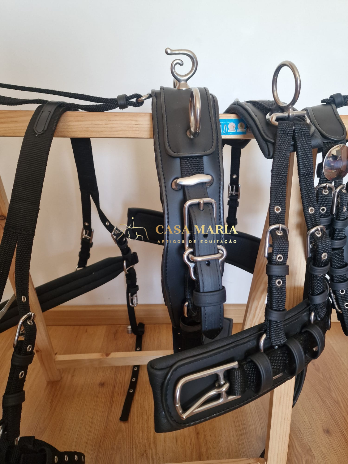 Arreios de equitação pretos com metal prateado pendurados num suporte de madeira