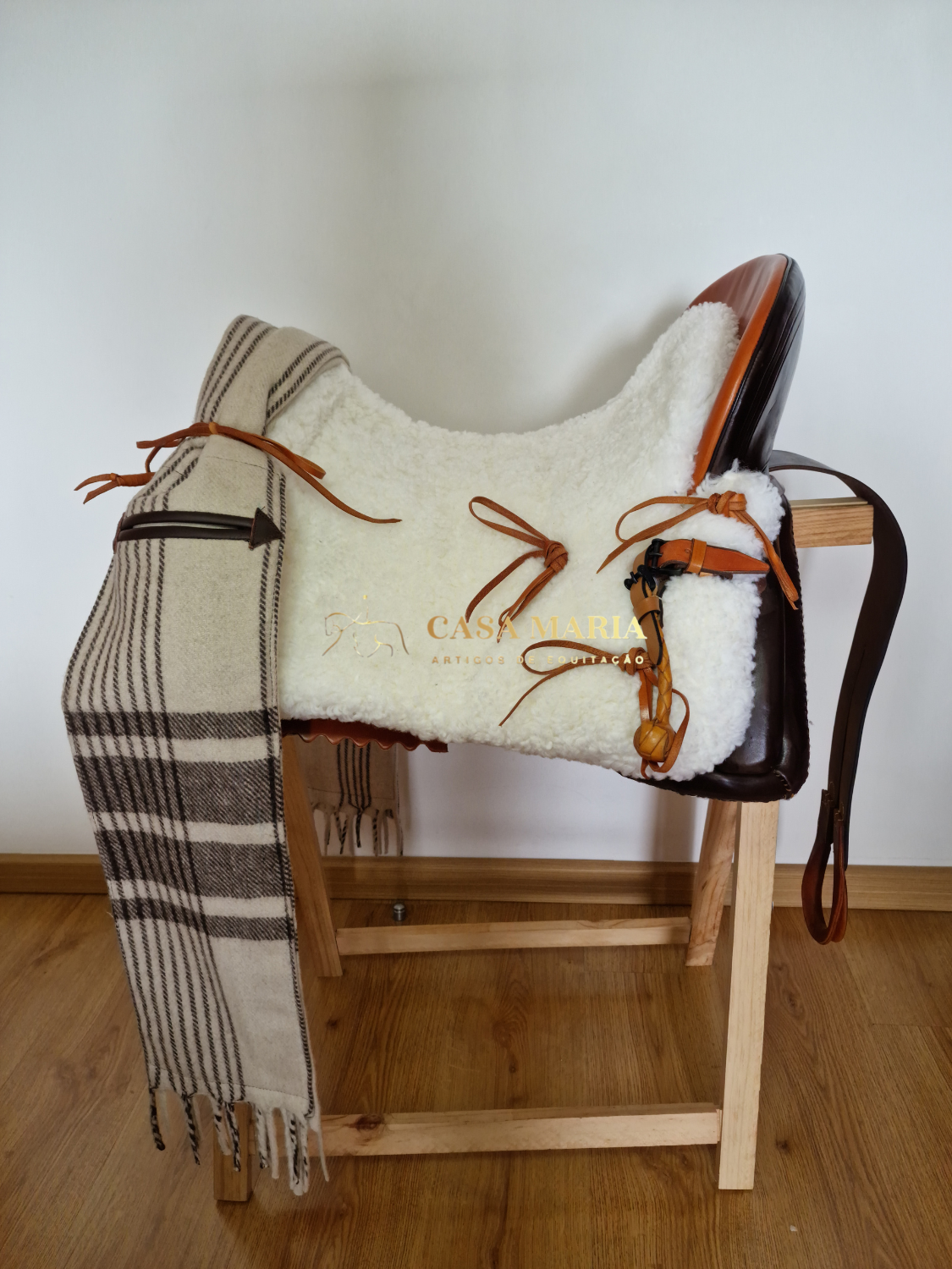 Sela de equitação em couro castanho com almofada branca felpuda e manta castanha e bege pendurada