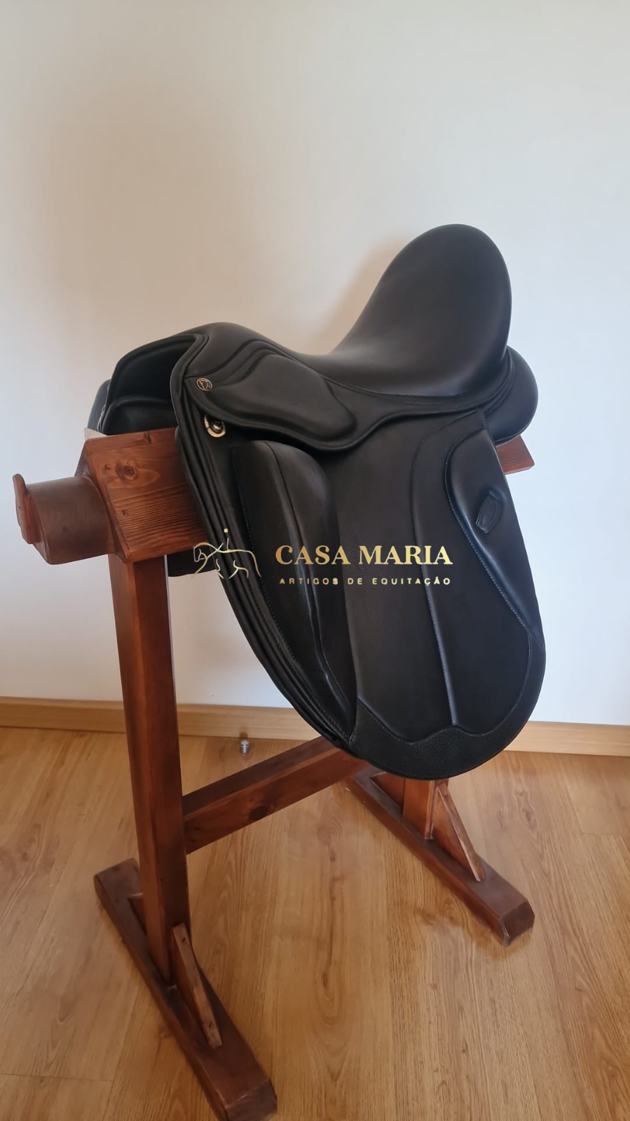 Sela de equitação preta de couro sobre suporte de madeira com texto CASA MARIA ARTIGOS DE EQUITAÇÃO