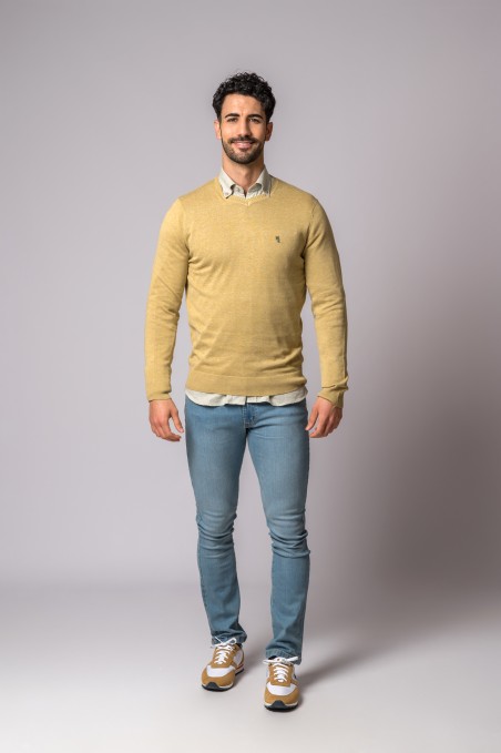 Homem vestido com camisola amarela, camisa branca, calças de ganga azul e sapatilhas brancas e bege.