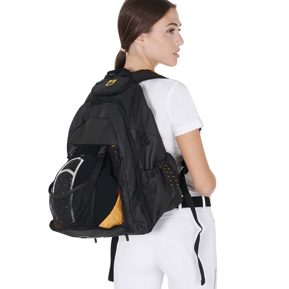 Mochila preta com bolso em rede e detalhes amarelos numa mulher com roupa branca