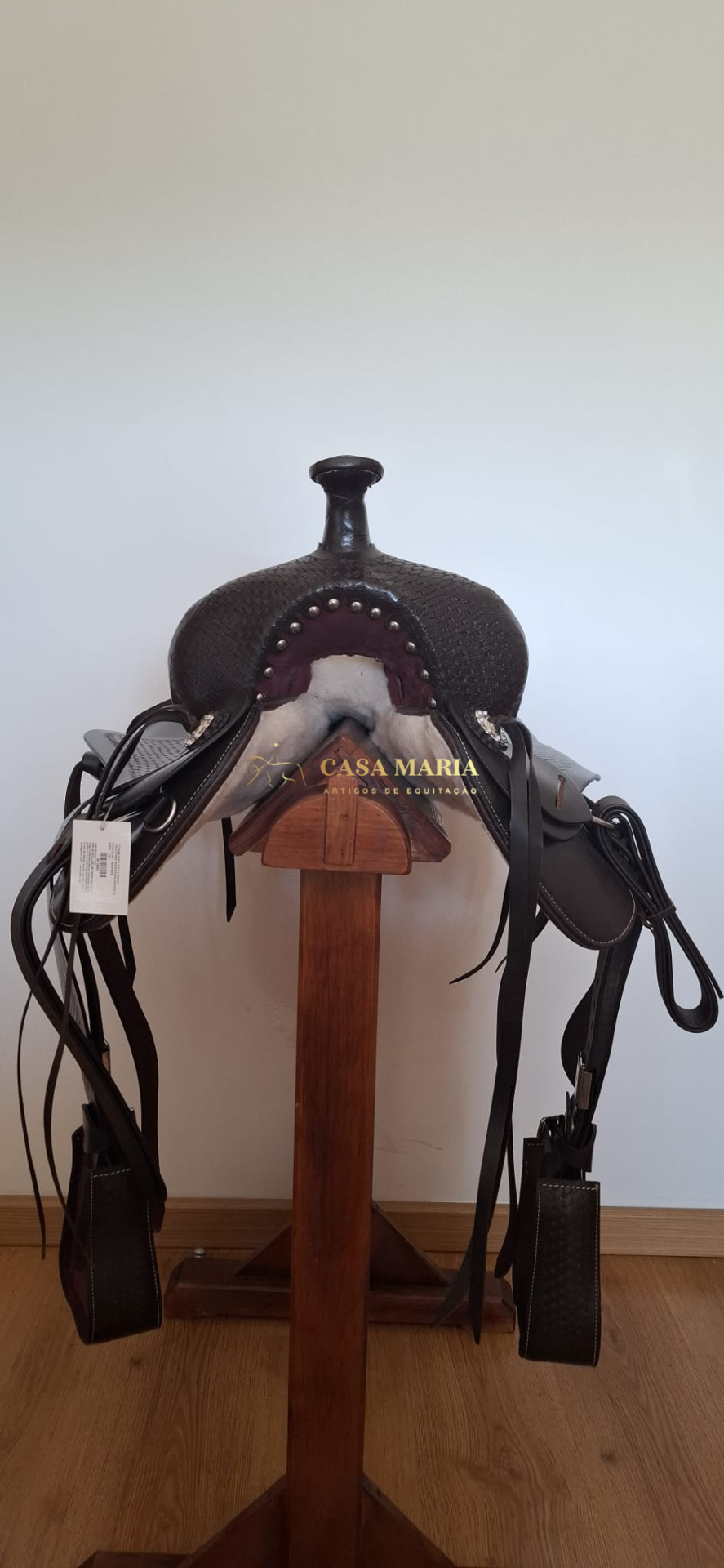 Sela de equitação preta com detalhes metálicos em suporte de madeira