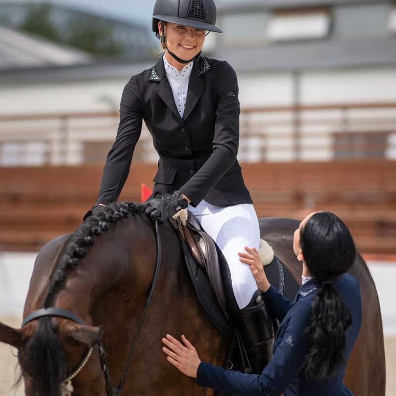 Jovem cavaleira com roupa de competição montada num cavalo castanho escuro numa pista de equitação