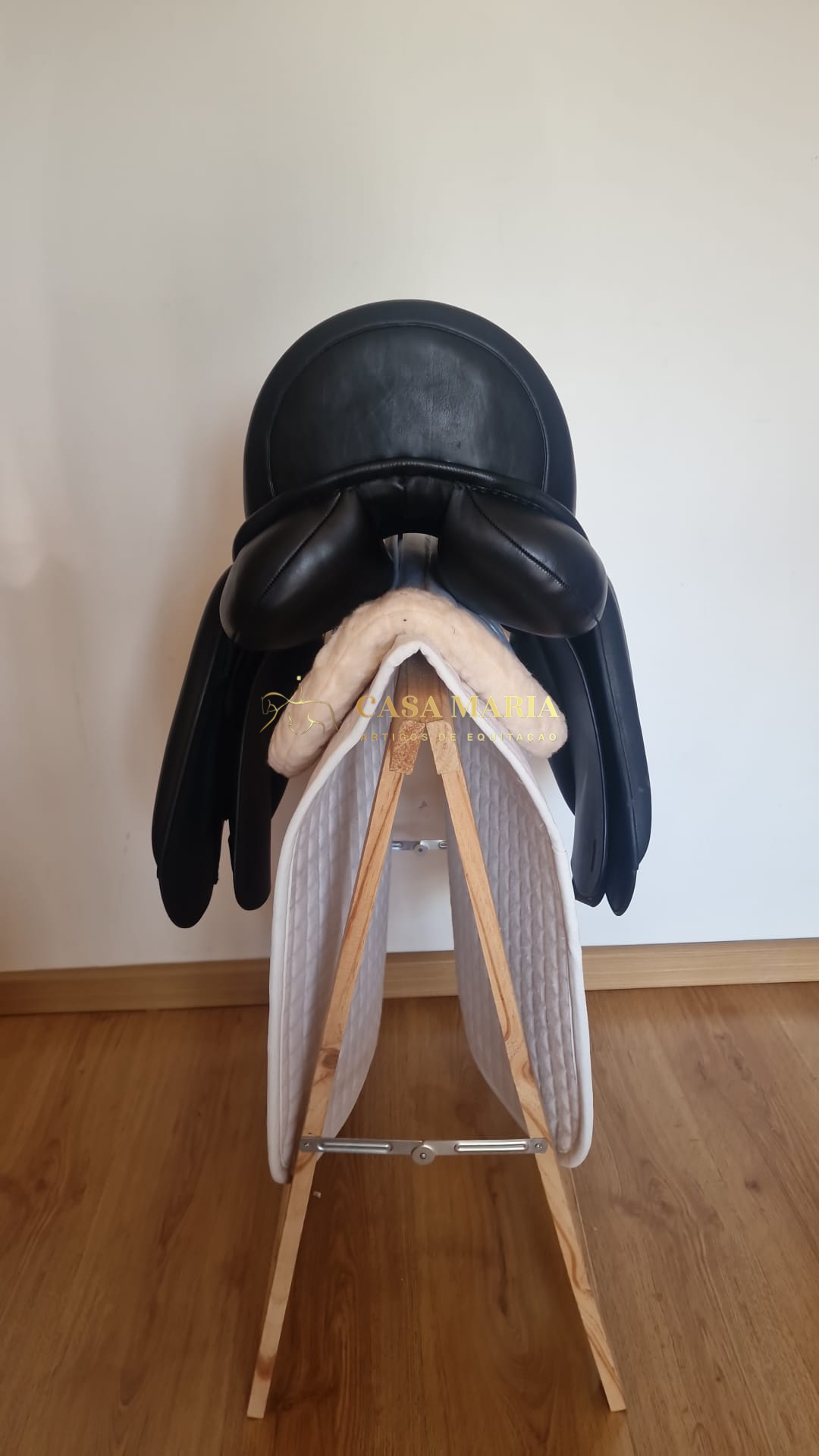 Sela de equitação preta sobre estrutura de madeira com manta branca