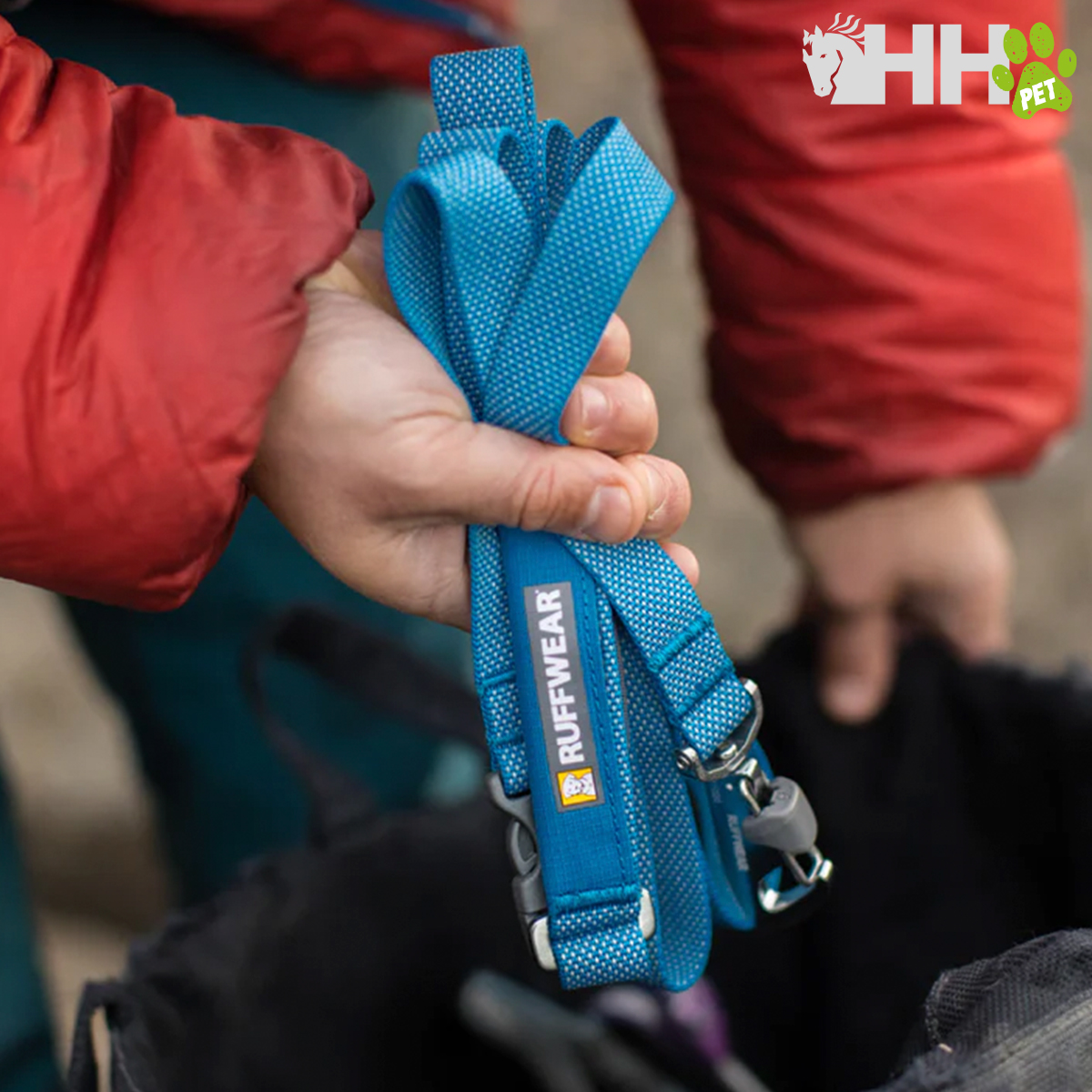 Trela azul para cão com etiqueta RUFFWEAR na mão de pessoa com casaco vermelho