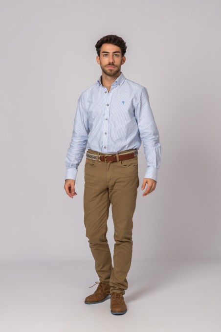 Homem com camisa azul clara às riscas, calças castanhas e sapatos castanhos em fundo cinza