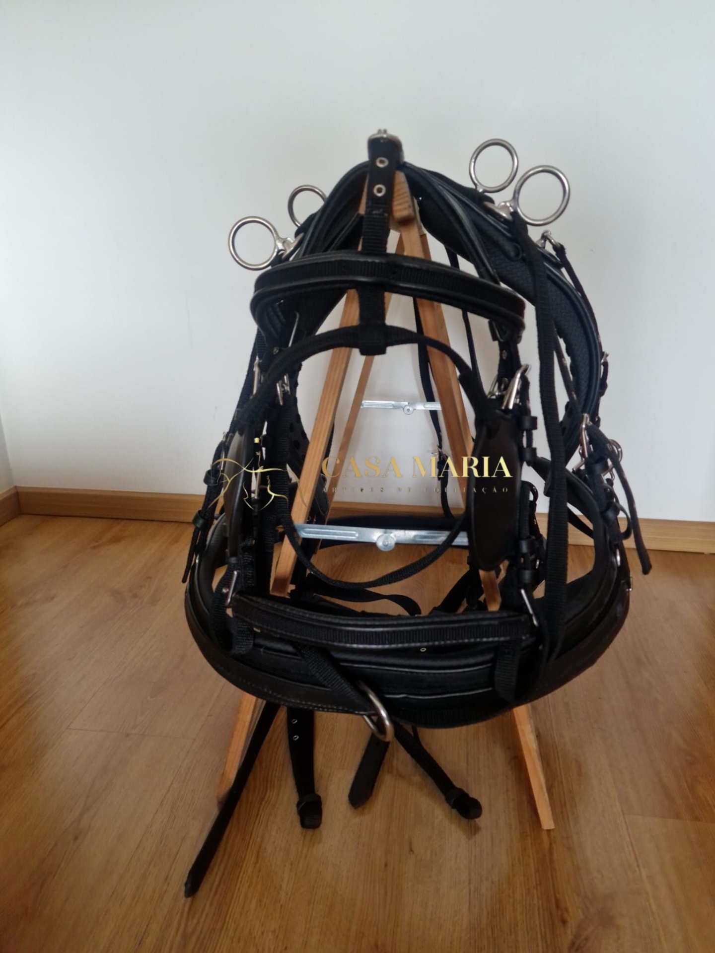 Bridão preto de cabedal com argolas metálicas pendurado em estrutura de madeira