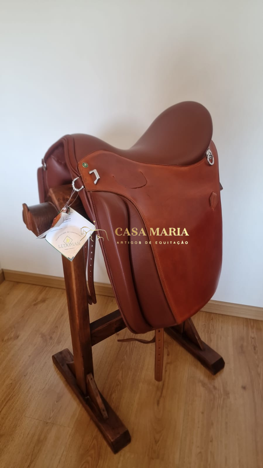 Sela de equitação castanha em suporte de madeira com etiqueta da marca Ludomar