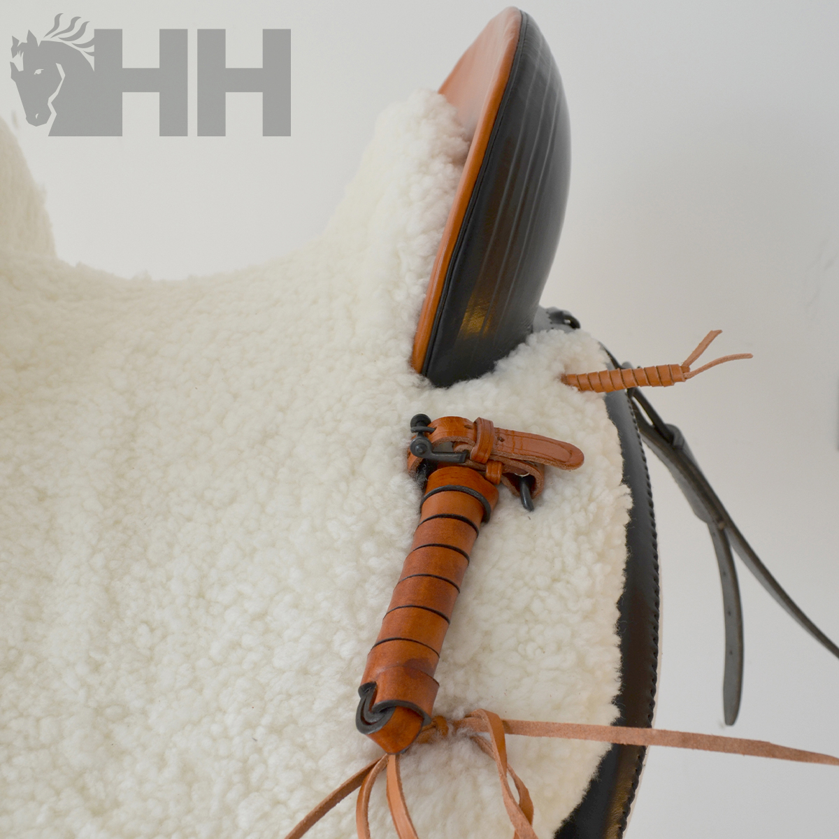 Sela de equitação com forro de lã branca e detalhes em couro castanho com logótipo HH cinza no fundo