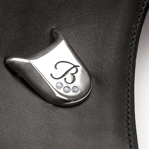 Detalhe em metal prateado com letra B e cristais em produto de couro preto